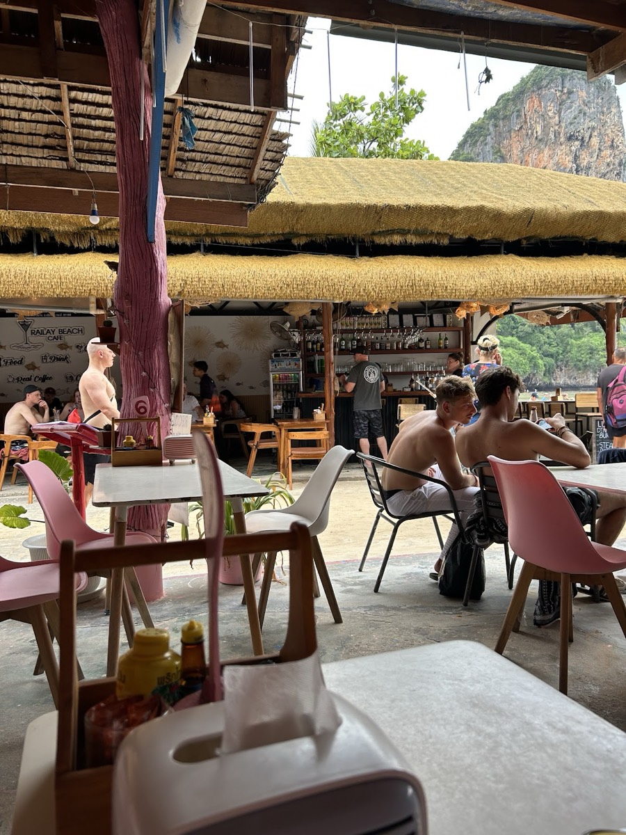 Thatched open-air seating at Railay Beach Cafe with the limestone cliff behind